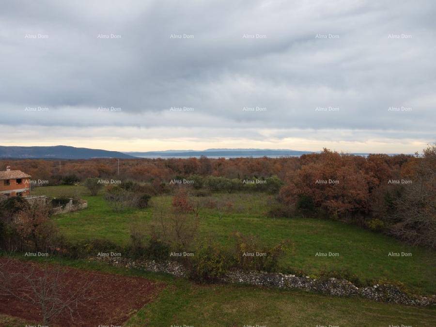 Blick auf eine weite grüne Landschaft mit Bäumen und einem entfernten Meer unter bewölktem Himmel.