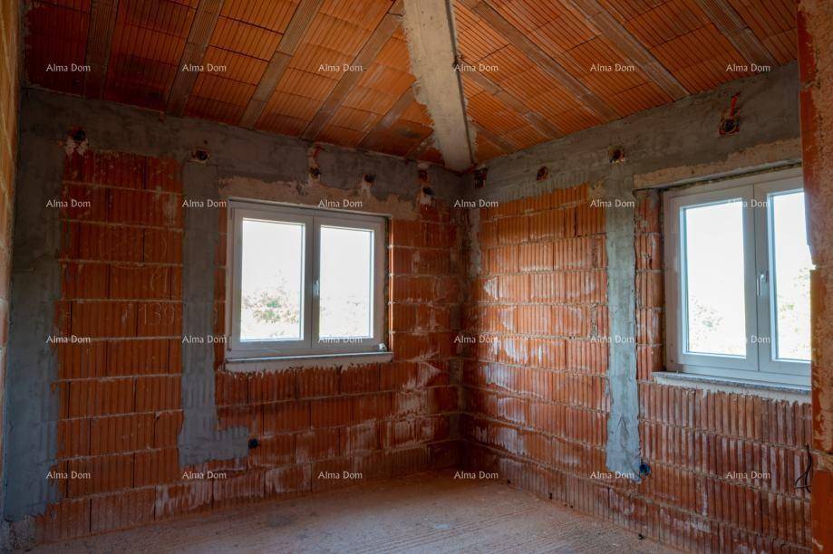 Raum im Rohbau mit Ziegelwänden und zwei Fenstern, die Tageslicht hereinlassen.