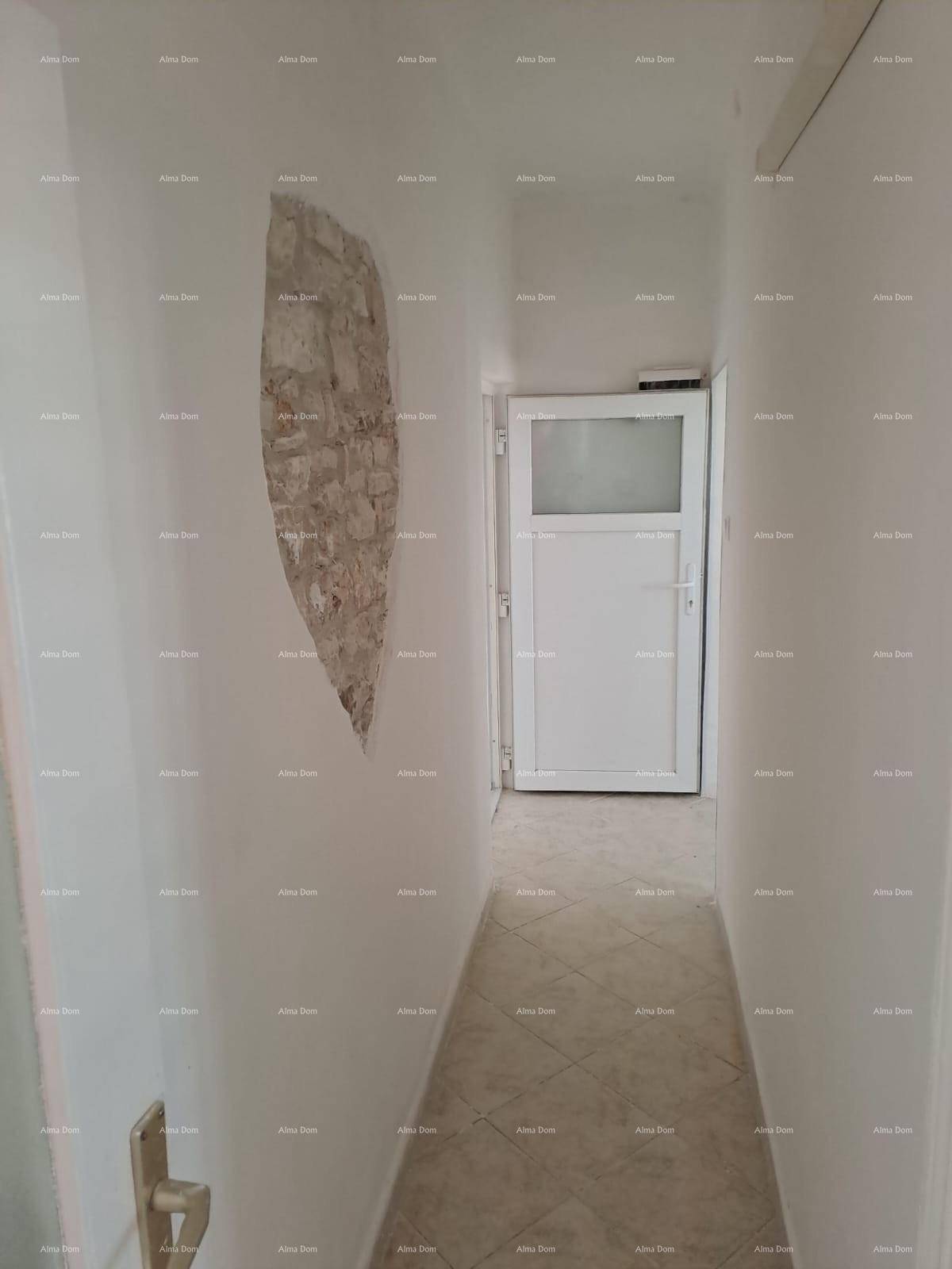 Schmaler Flur mit Fliesenboden und einem dekorativen Stück freigelegter Steinwand.