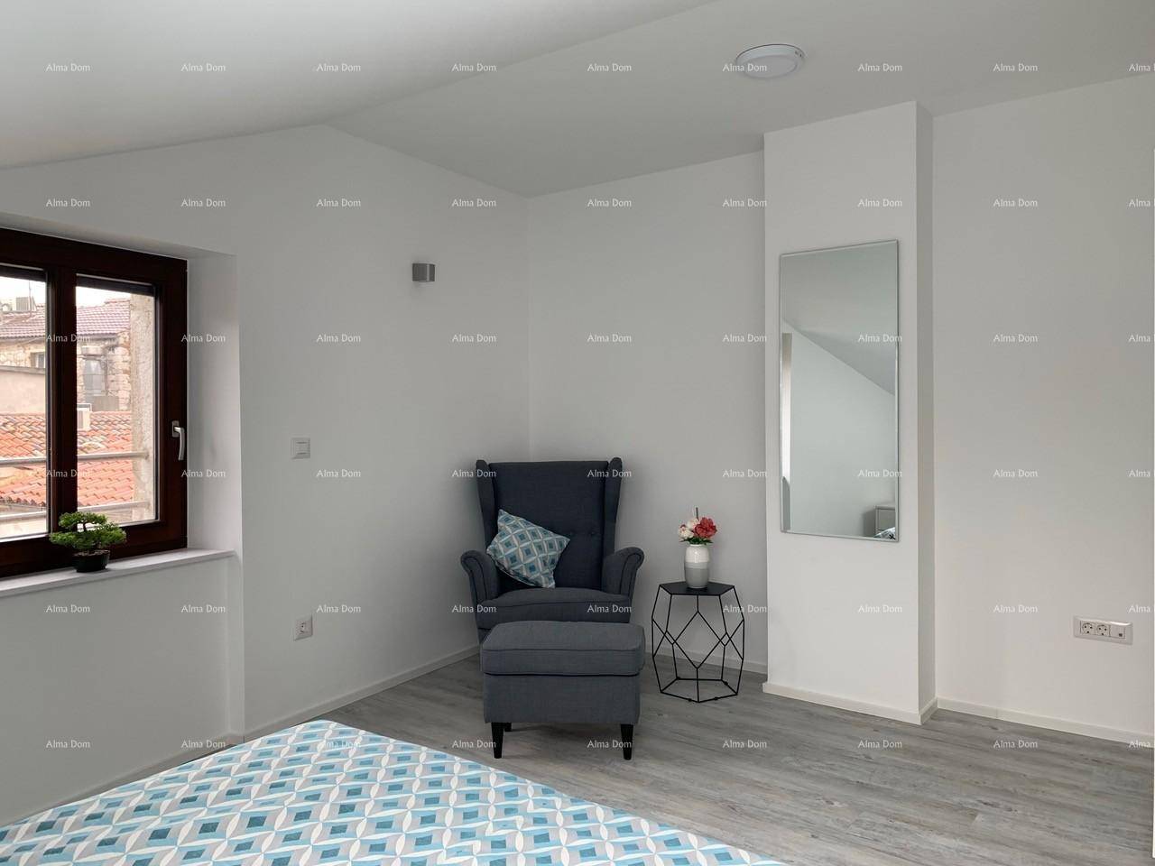 Schlafzimmer mit Fenster, bequemem Sessel, Fußhocker und einem großen Wandspiegel.