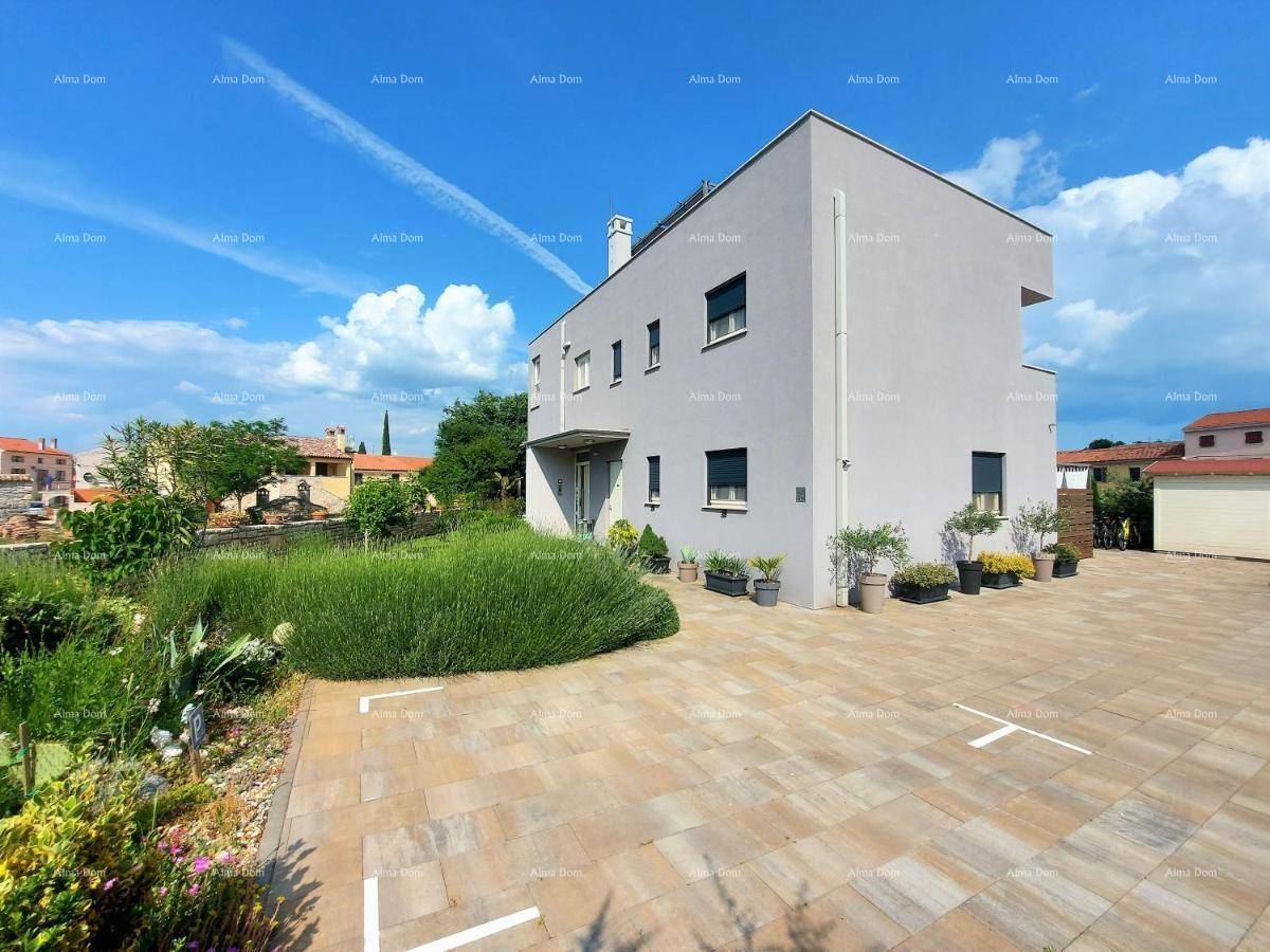 Moderne Hausfassade mit gepflastertem Parkplatz und mediterraner Bepflanzung im Vordergrund.