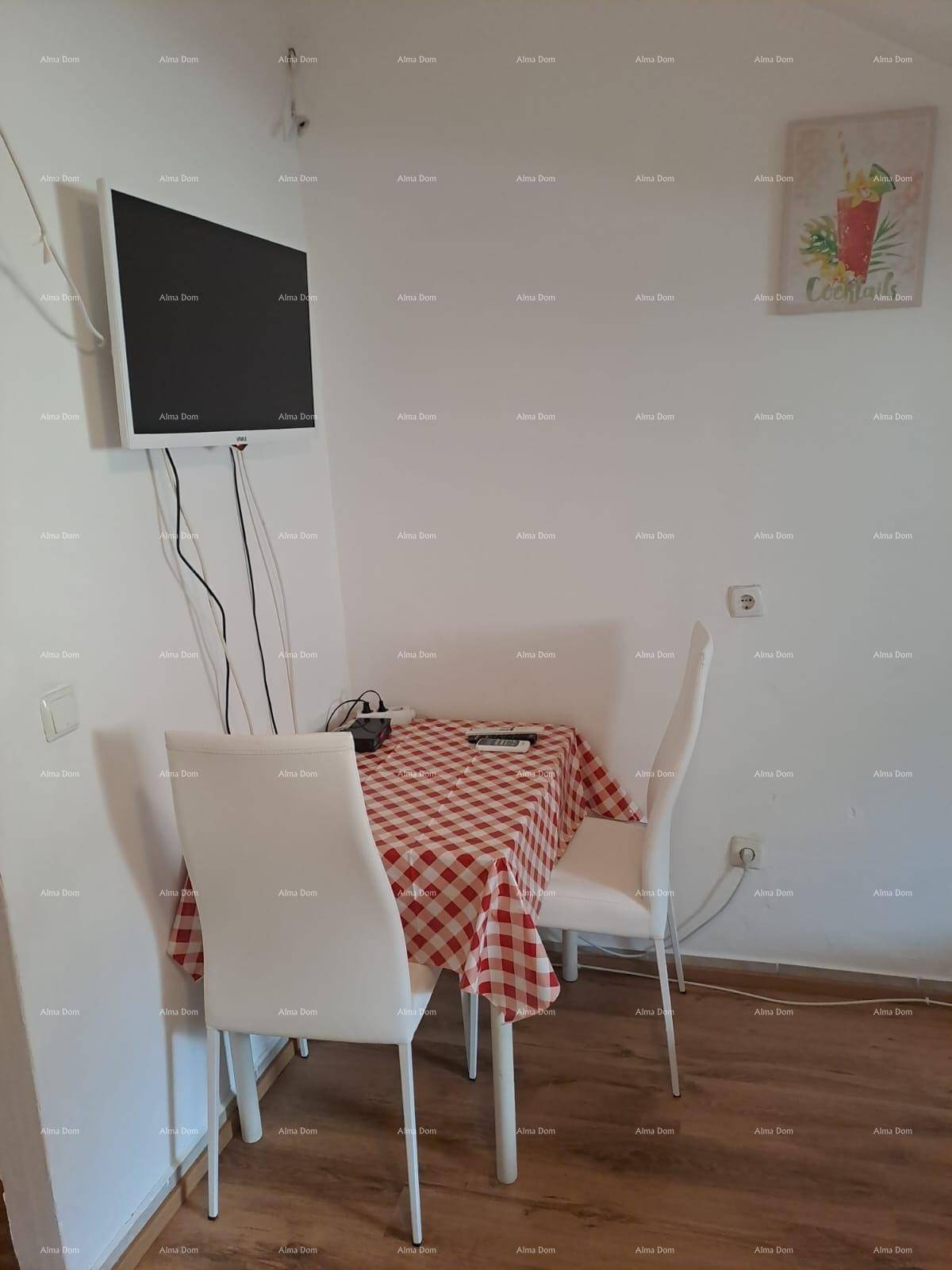 Kleiner Essbereich mit karierter Tischdecke und Wandfernseher, ideal für Mahlzeiten.