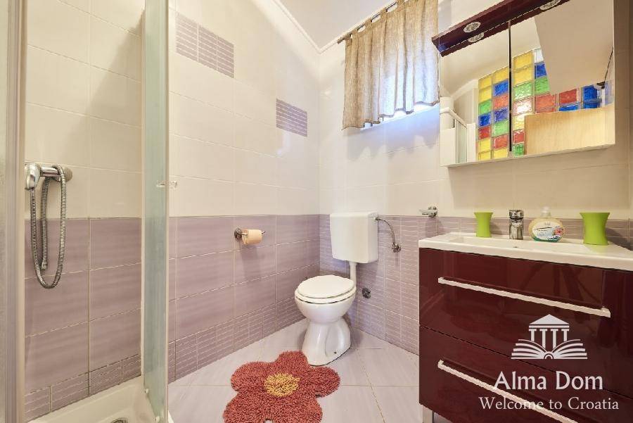 Badezimmer mit Dusche, WC und farbenfrohen Glasbausteinen im Spiegelschrank.