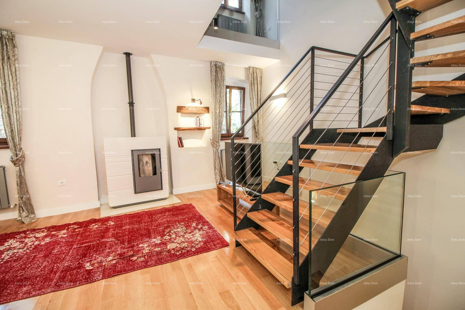 Wohnzimmer mit modernem Kaminofen, Holzboden und einer eleganten Treppe mit Glasgeländer.