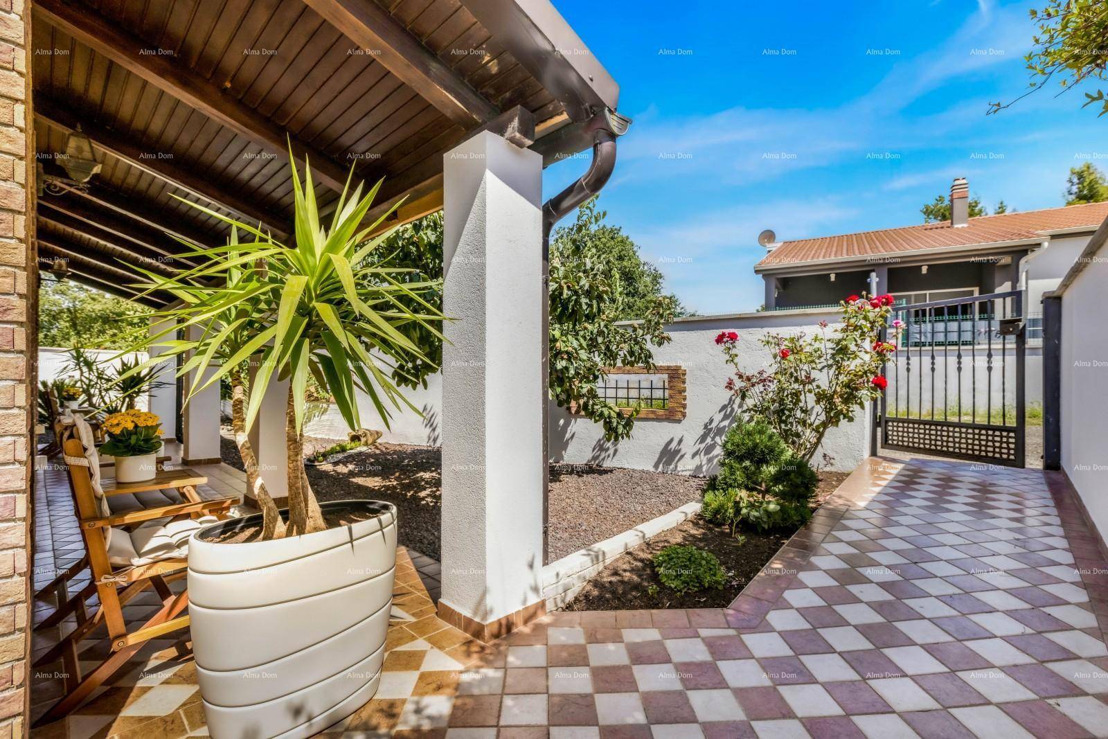 Überdachte Terrasse mit Säulen, Topfpflanzen und einem gepflasterten Bereich, der zum Garten führt.