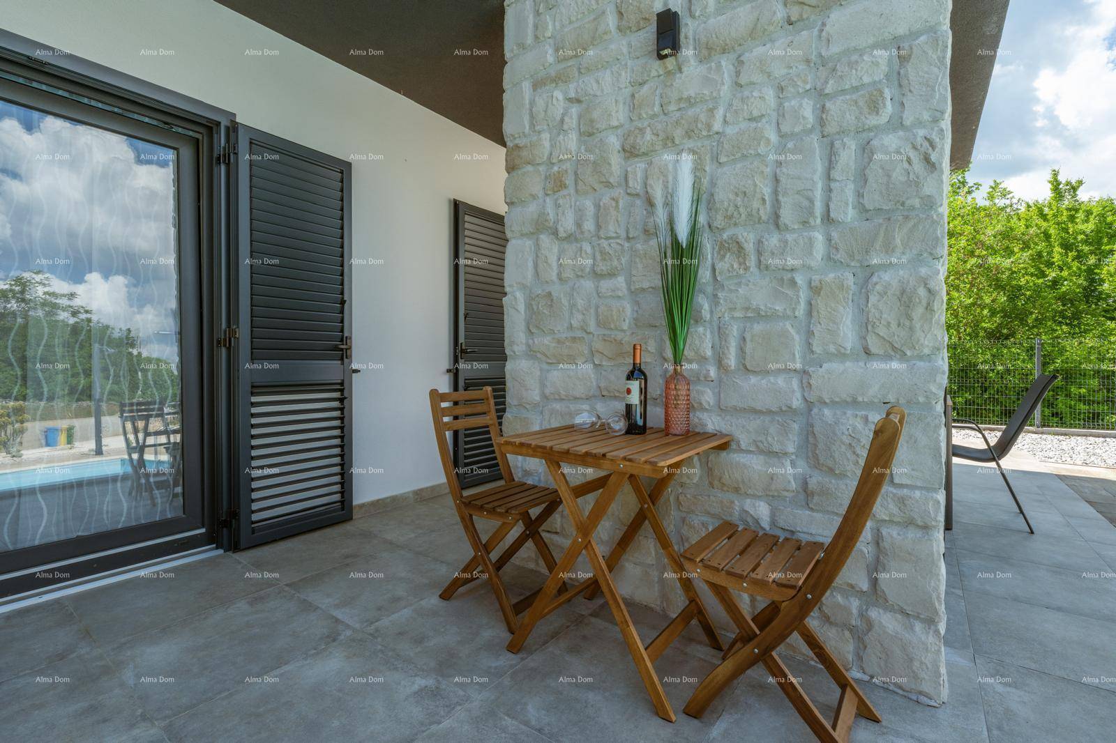 Gemütlicher Sitzbereich im Freien mit Holztisch und Stühlen neben einer Steinwand und dem Pool.