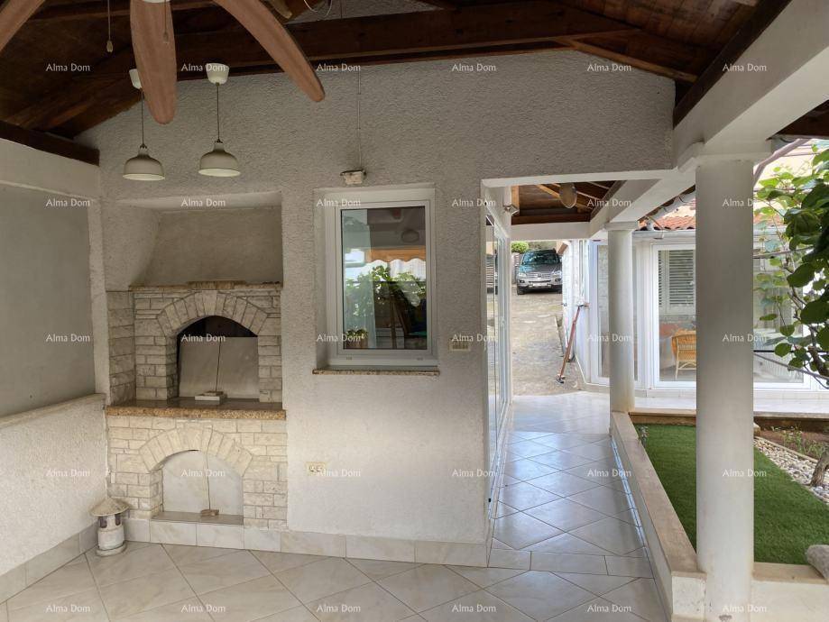 Überdachter Außenbereich mit gemauertem Grill, Fliesenboden und Holzbalkendecke.