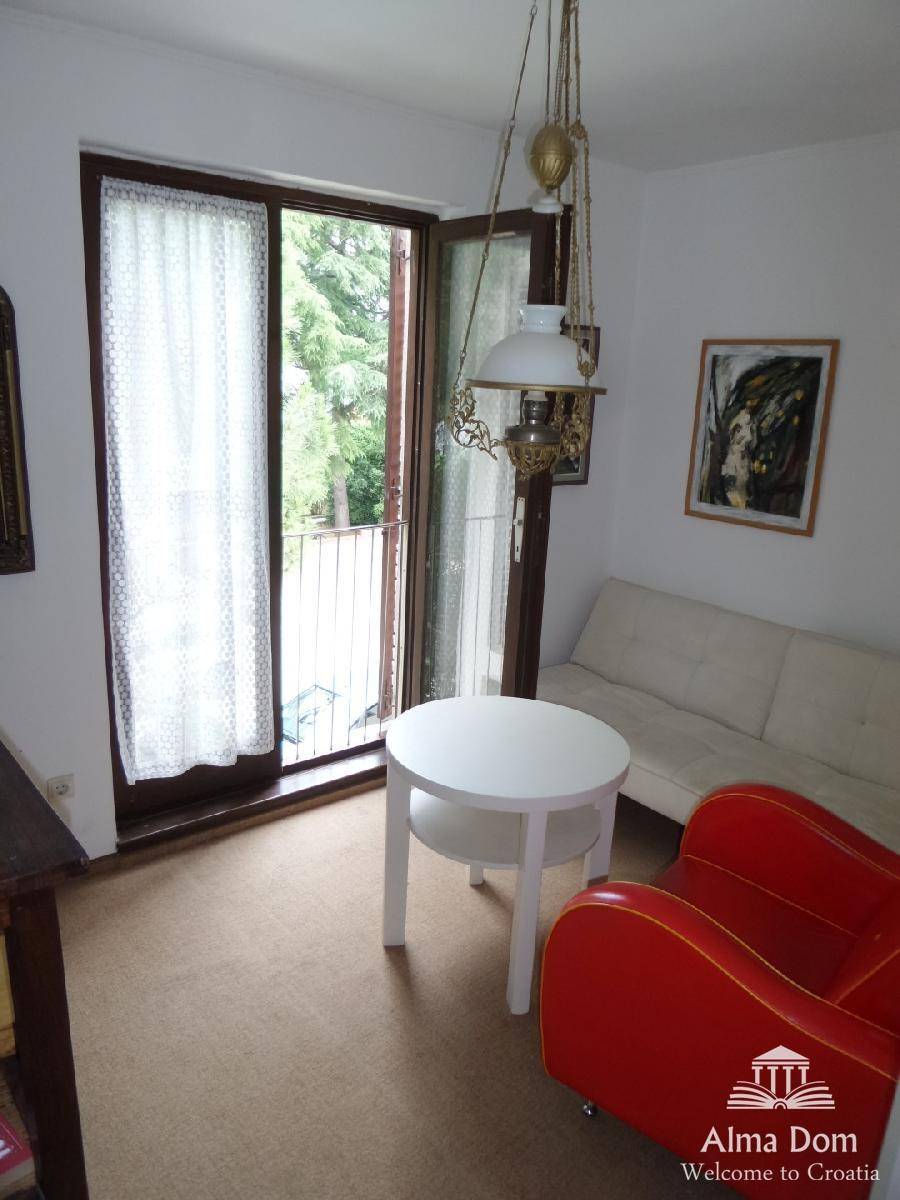 Kleines Wohnzimmer mit rotem Sessel, weißem Sofa und Zugang zu einem französischen Balkon, hell und gemütlich.