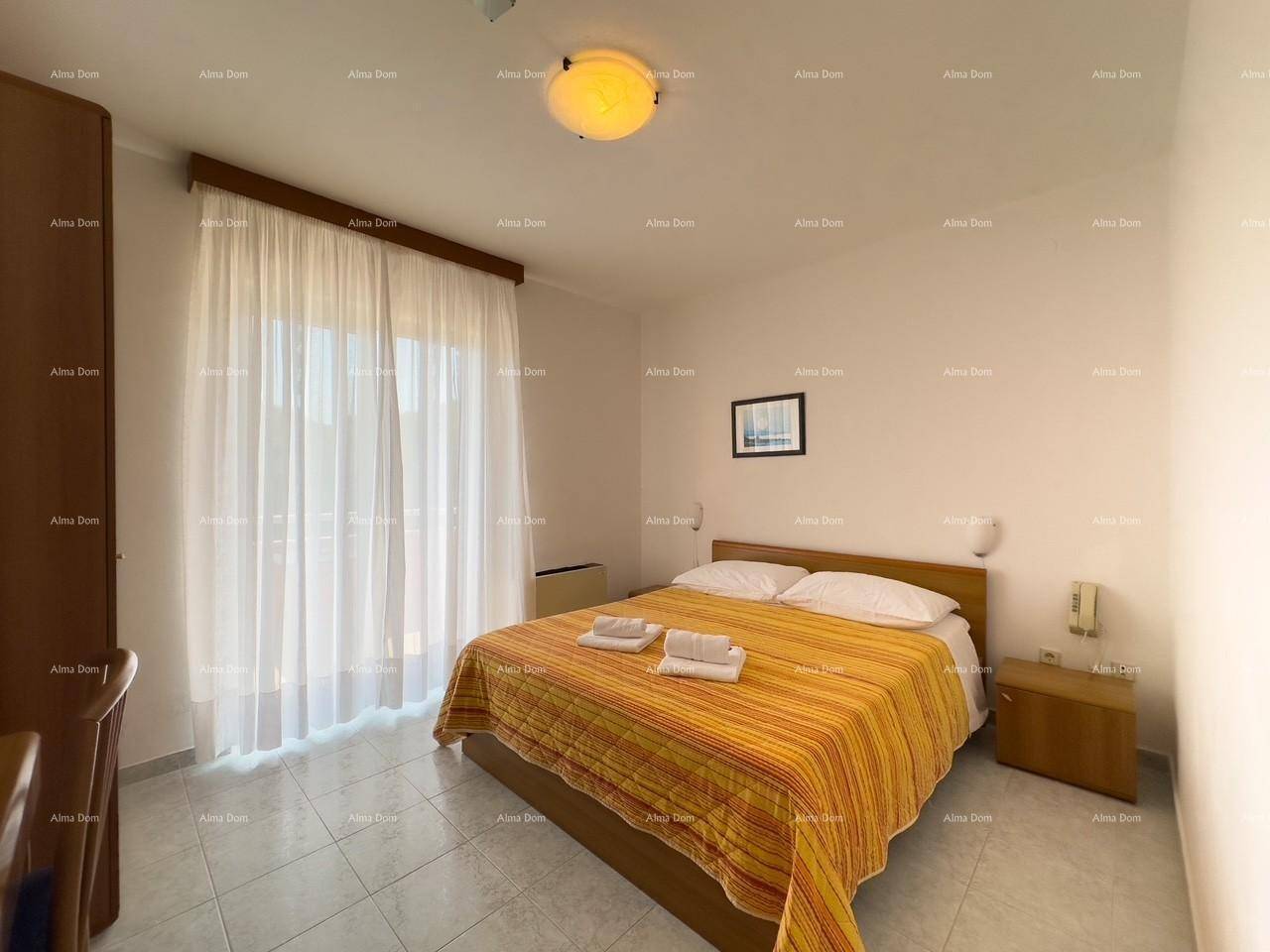 Helles Schlafzimmer mit Doppelbett, Fliesenboden und großen Fenstern mit Vorhängen.
