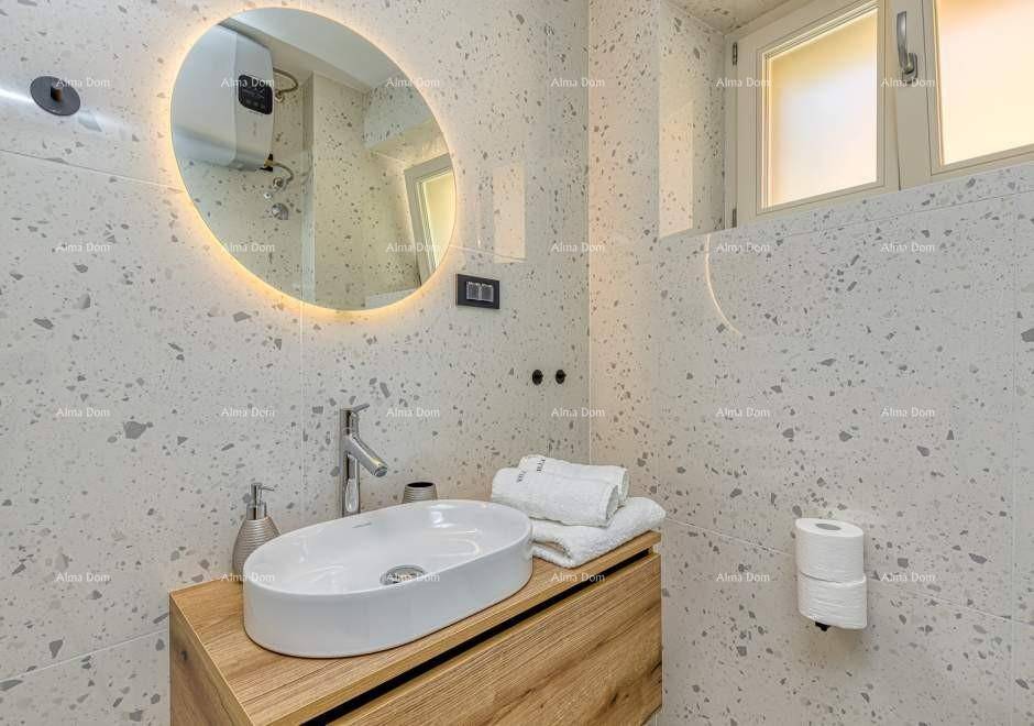 Modernes Badezimmer mit ovalem Waschbecken, beleuchtetem Spiegel und gesprenkelten Fliesen.