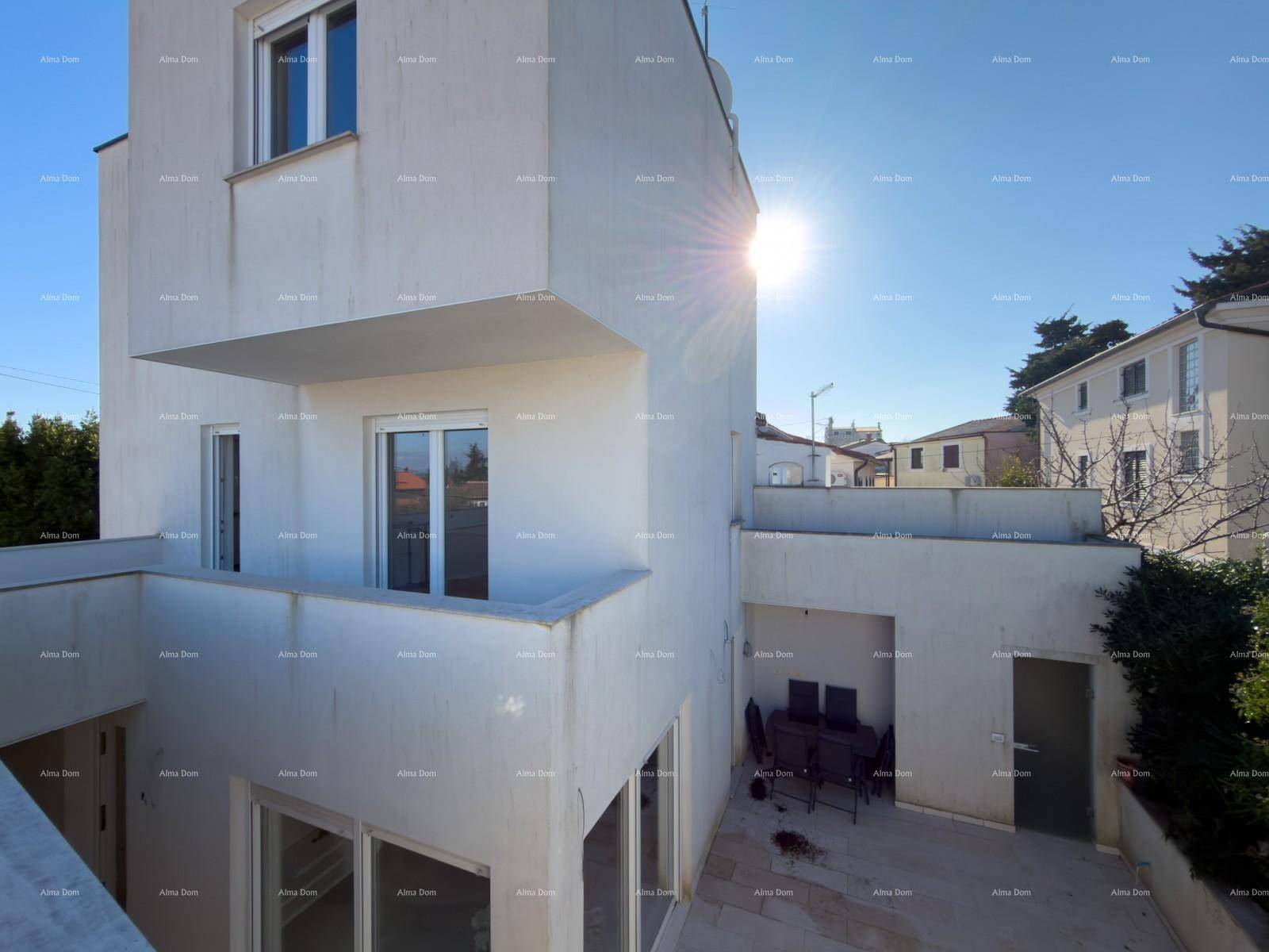 Moderne weiße Fassade eines Gebäudes mit Balkon und sonnigem Außenbereich im Erdgeschoss.
