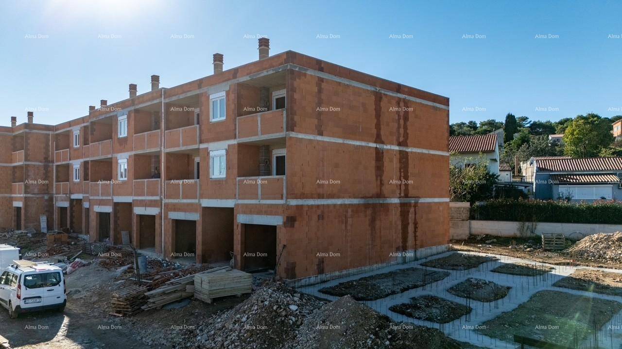 Gebäude im Rohbau mit orangefarbenen Ziegeln und Baustelle im Vordergrund unter blauem Himmel.