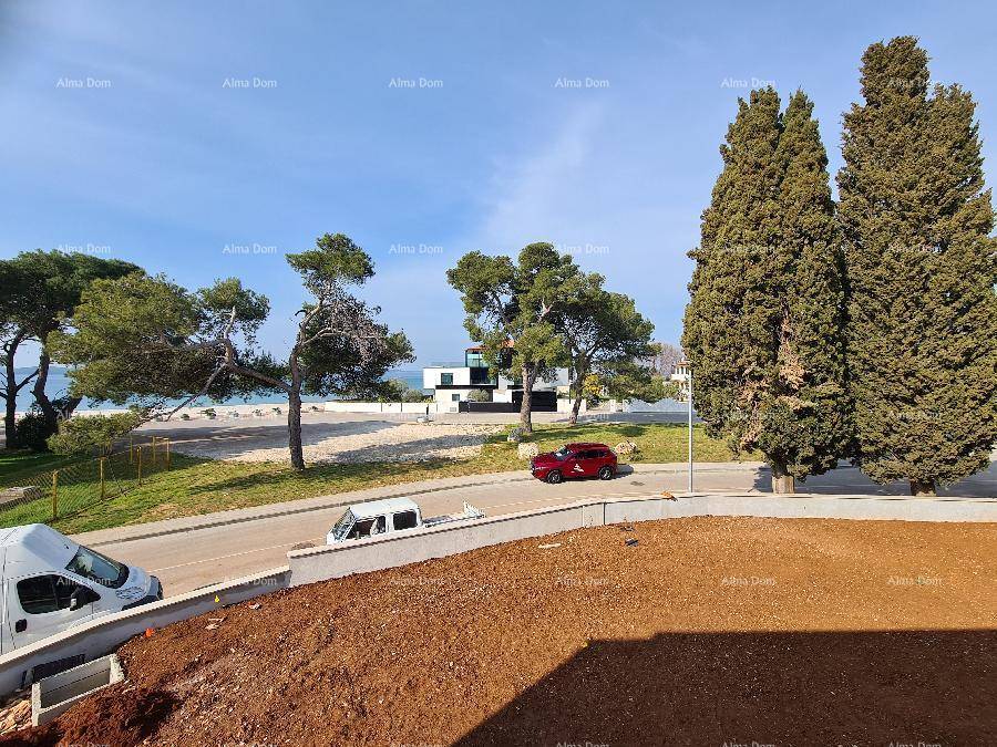 Panoramablick auf die Küste mit Meer, Strand und grünen Bäumen unter blauem Himmel.