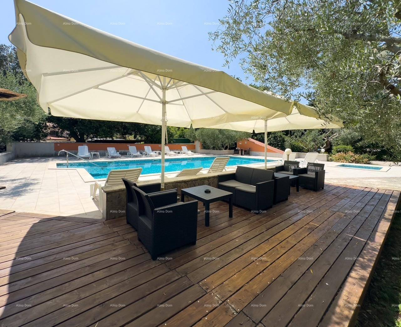 Großer Poolbereich mit Holzterrasse, Sitzgelegenheiten und Sonnenschirm, umgeben von Bäumen.