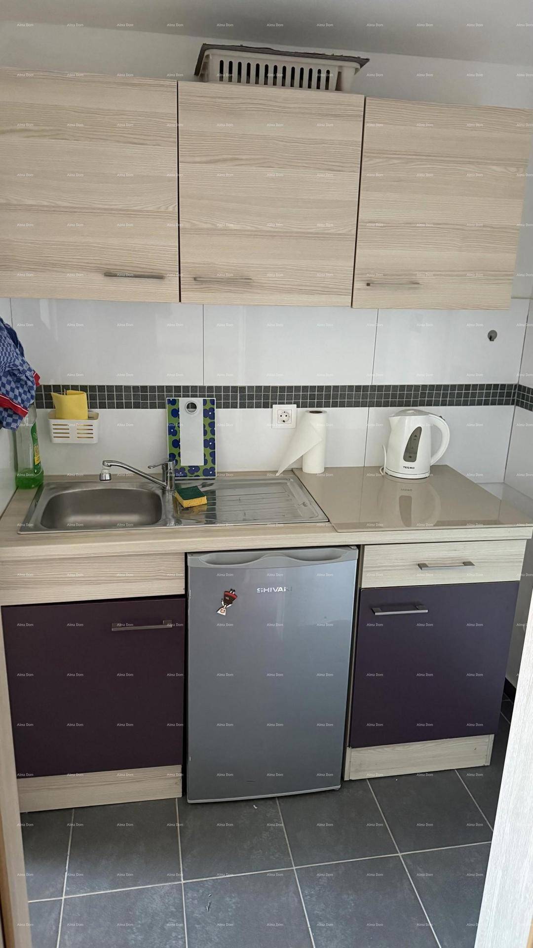 Kompakte Küchenzeile mit Spüle, Minikühlschrank und hellen Holzschränken.