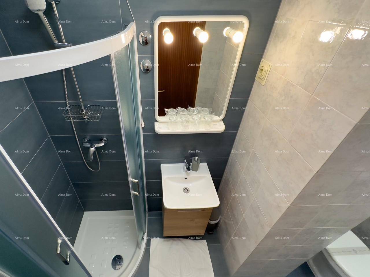 Badezimmer mit Duschkabine und Waschbecken, ausgestattet mit grauen Fliesen und einem Spiegel.