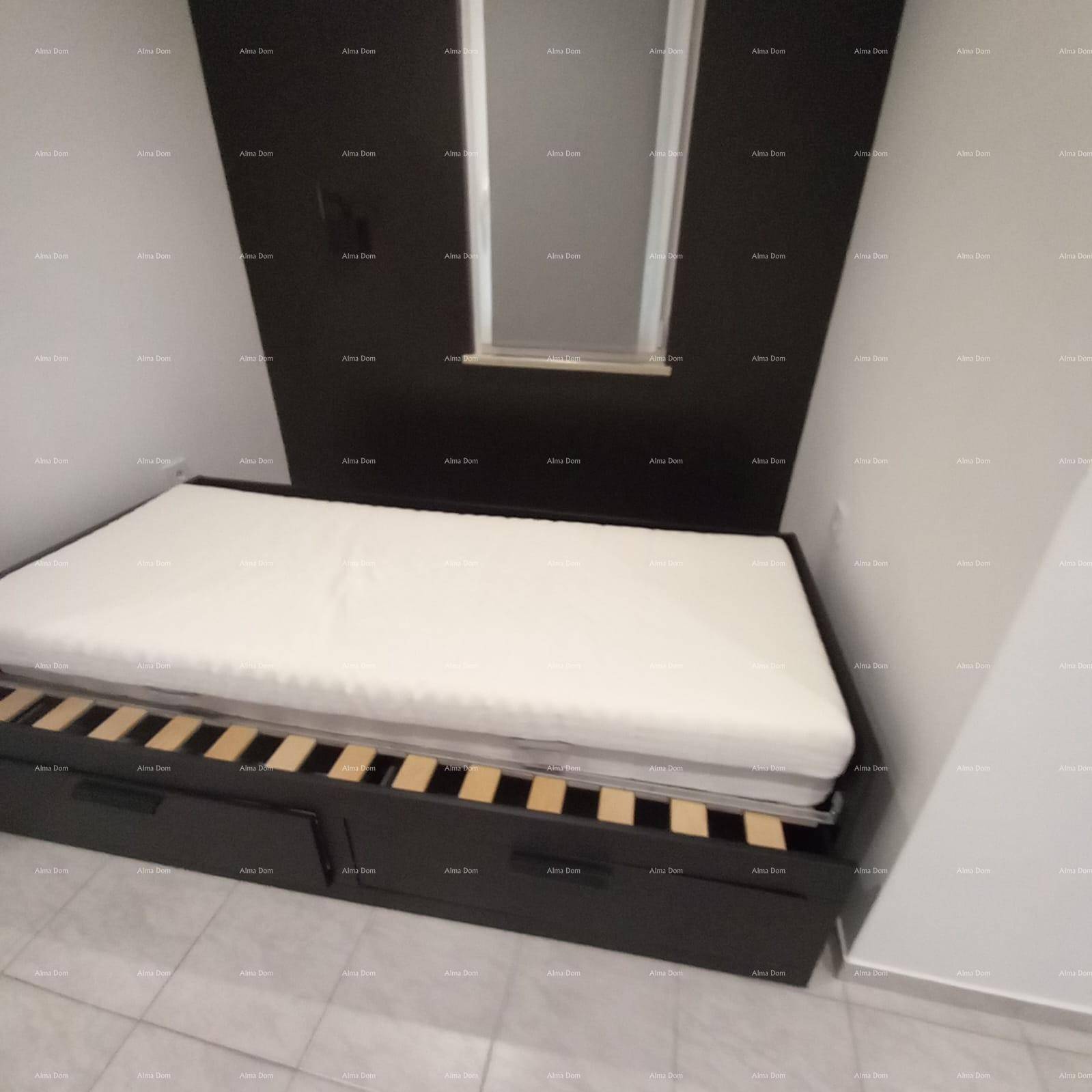 Schlafbereich mit einem Bett und integrierten Schubladen, vor einer dunklen Wand.