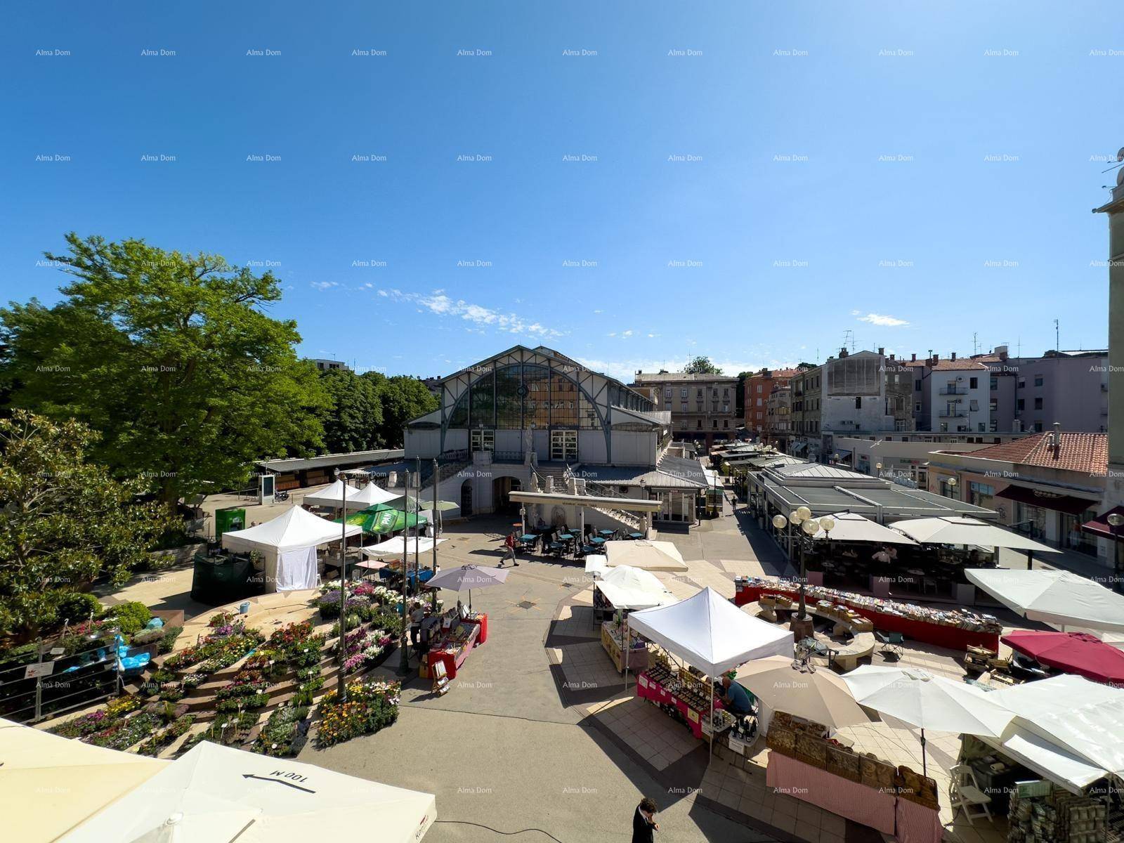 Weitläufiger Blick auf einen belebten Stadtplatz mit Marktständen und historischer Markthalle.