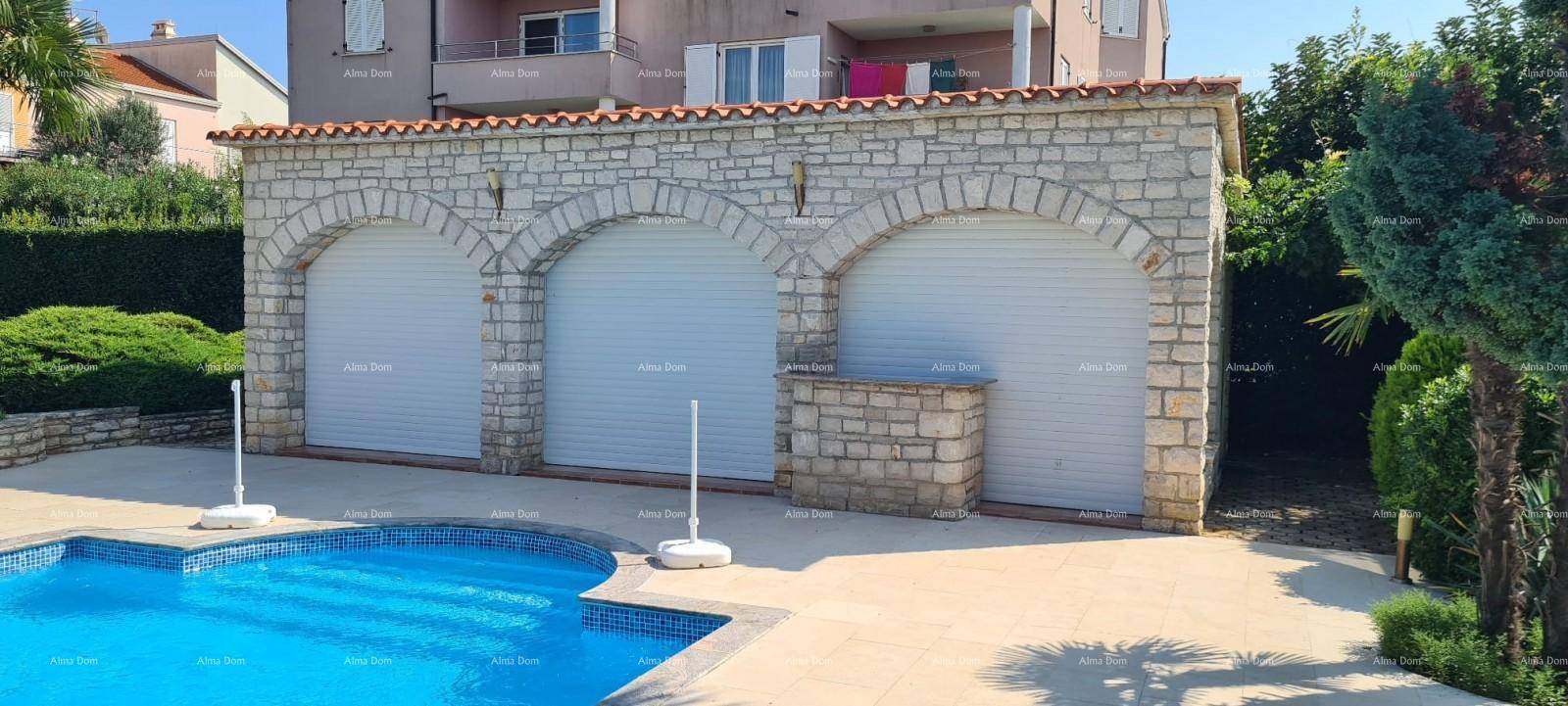 Steinernes Garagengebäude mit drei Rolltoren und direkt angrenzendem, blauem Swimmingpool.