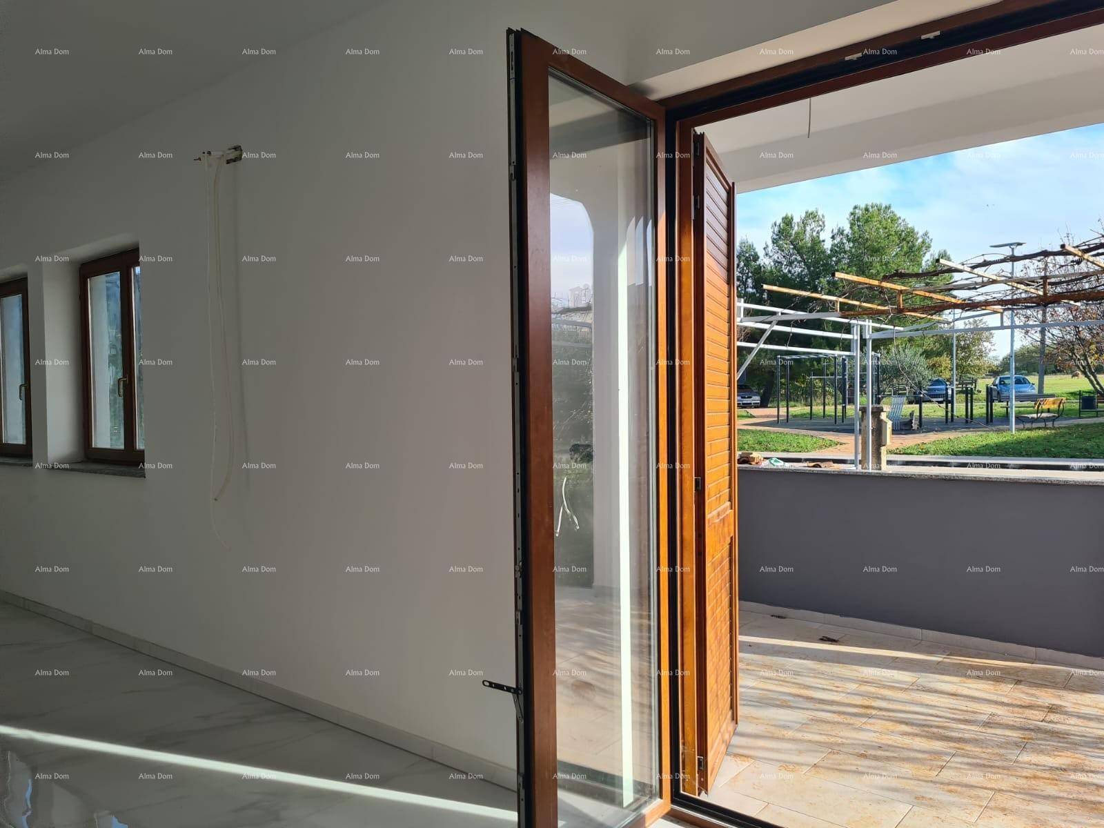 Heller Wohnbereich mit großem Fenster und Zugang zu einer überdachten Außenterrasse.