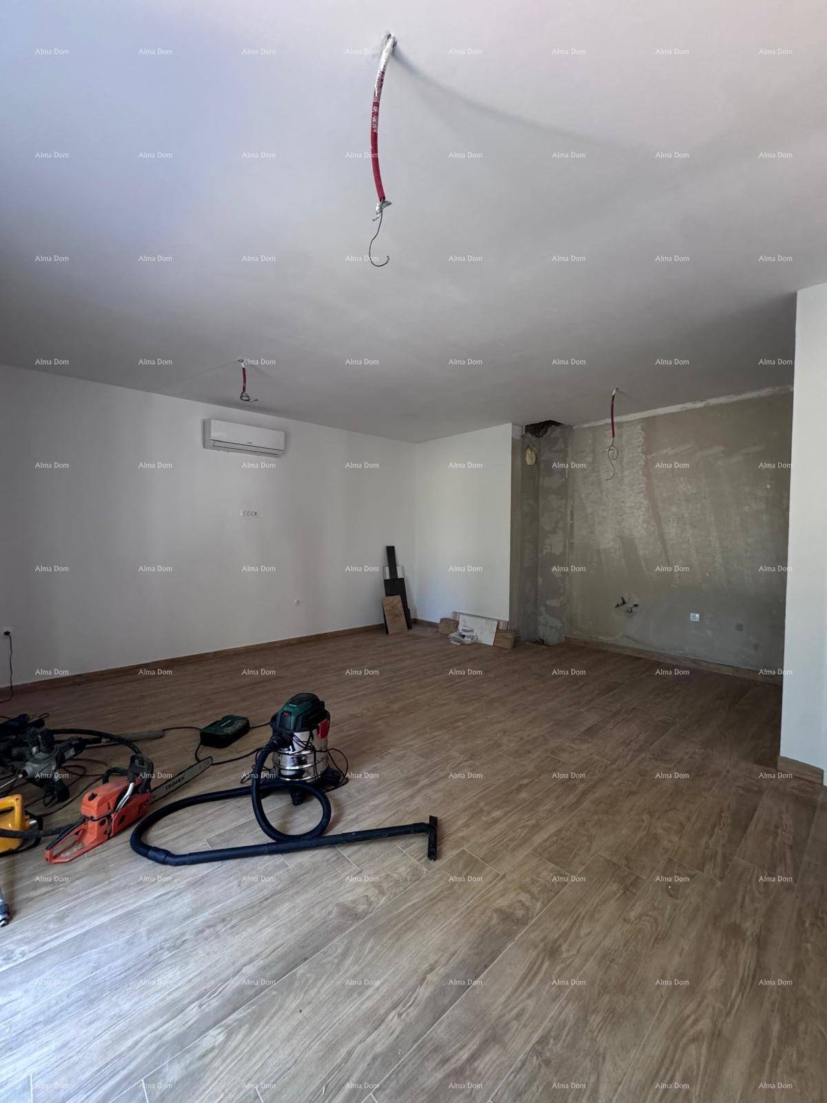 Geräumiger Wohnraum im Rohbau mit Holzboden, Klimaanlage und teilweise unverputzten Wänden.