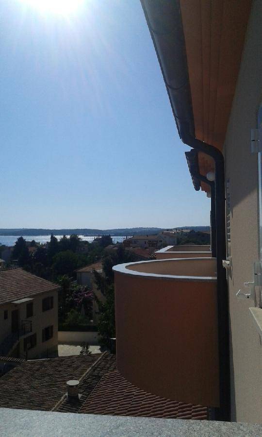 Blick von einem Balkon auf das Meer und die umliegende Stadt mit roten Dächern.