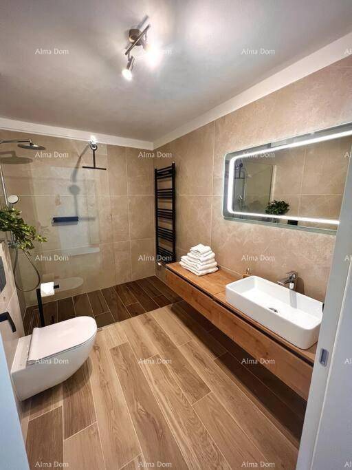 Zeitgemäßes Badezimmer mit beleuchtetem Spiegel, Holzwaschtisch und geräumiger Dusche.