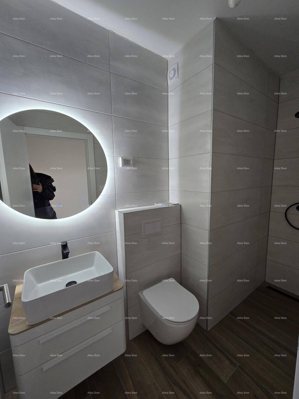 Modernes Badezimmer mit grauen Fliesen, beleuchtetem Spiegel und stilvollem Waschtisch mit Unterschrank.