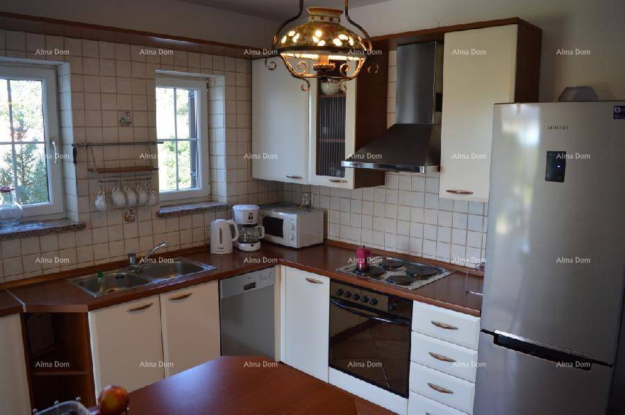 Funktionale Küche mit hellen Schränken, Fliesenboden und Blick ins Grüne durch zwei Fenster.