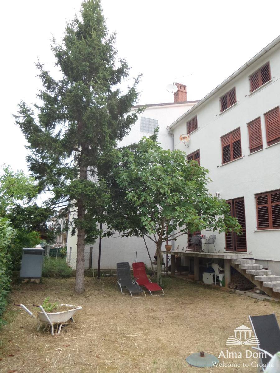 Rückansicht des Hauses mit Garten, hohen Bäumen und Liegestühlen im Freien für sonnige Tage.