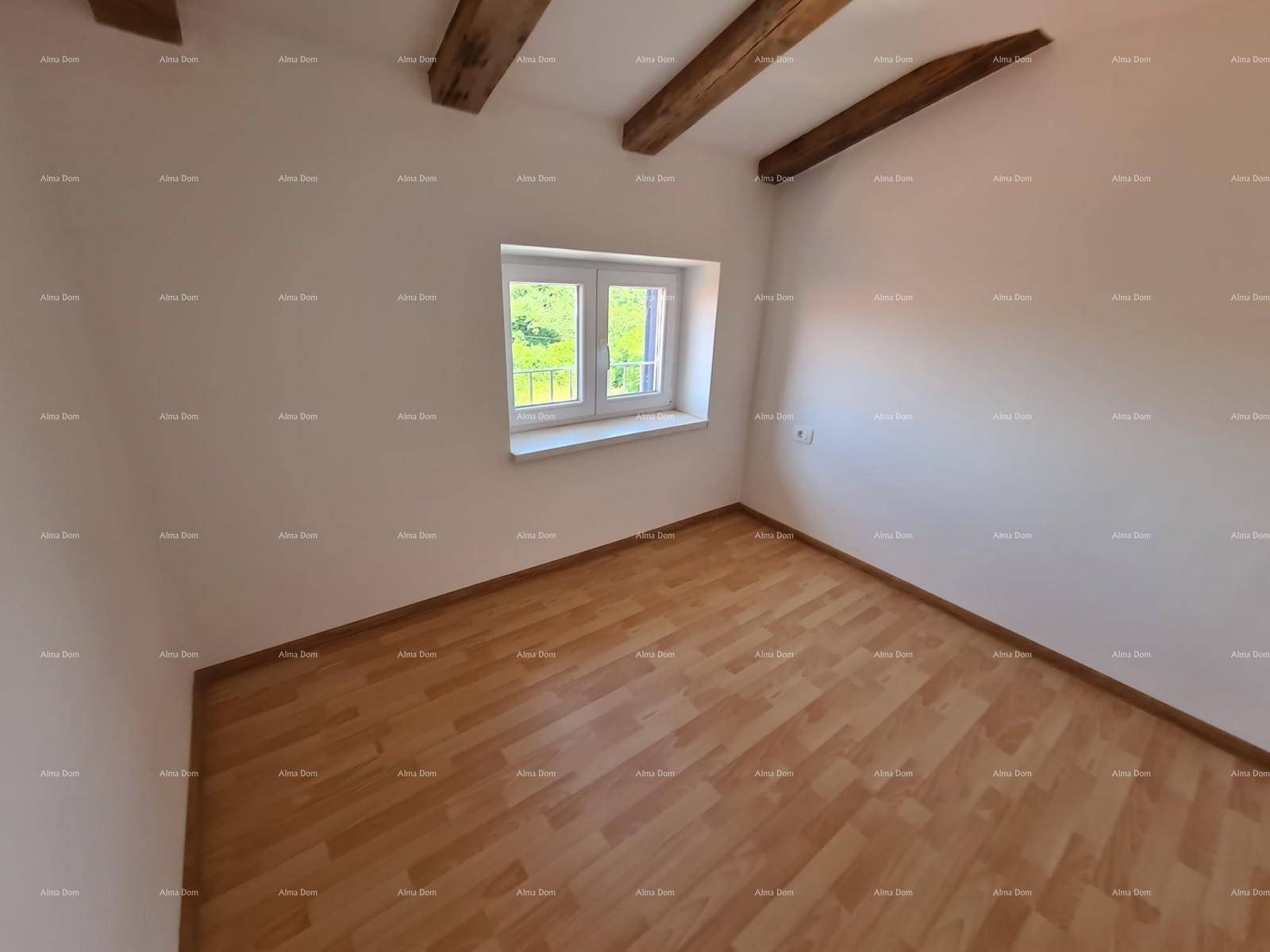 Helles Zimmer mit sichtbaren Holzbalken, Laminatboden und einem Fenster mit Blick ins Grüne.
