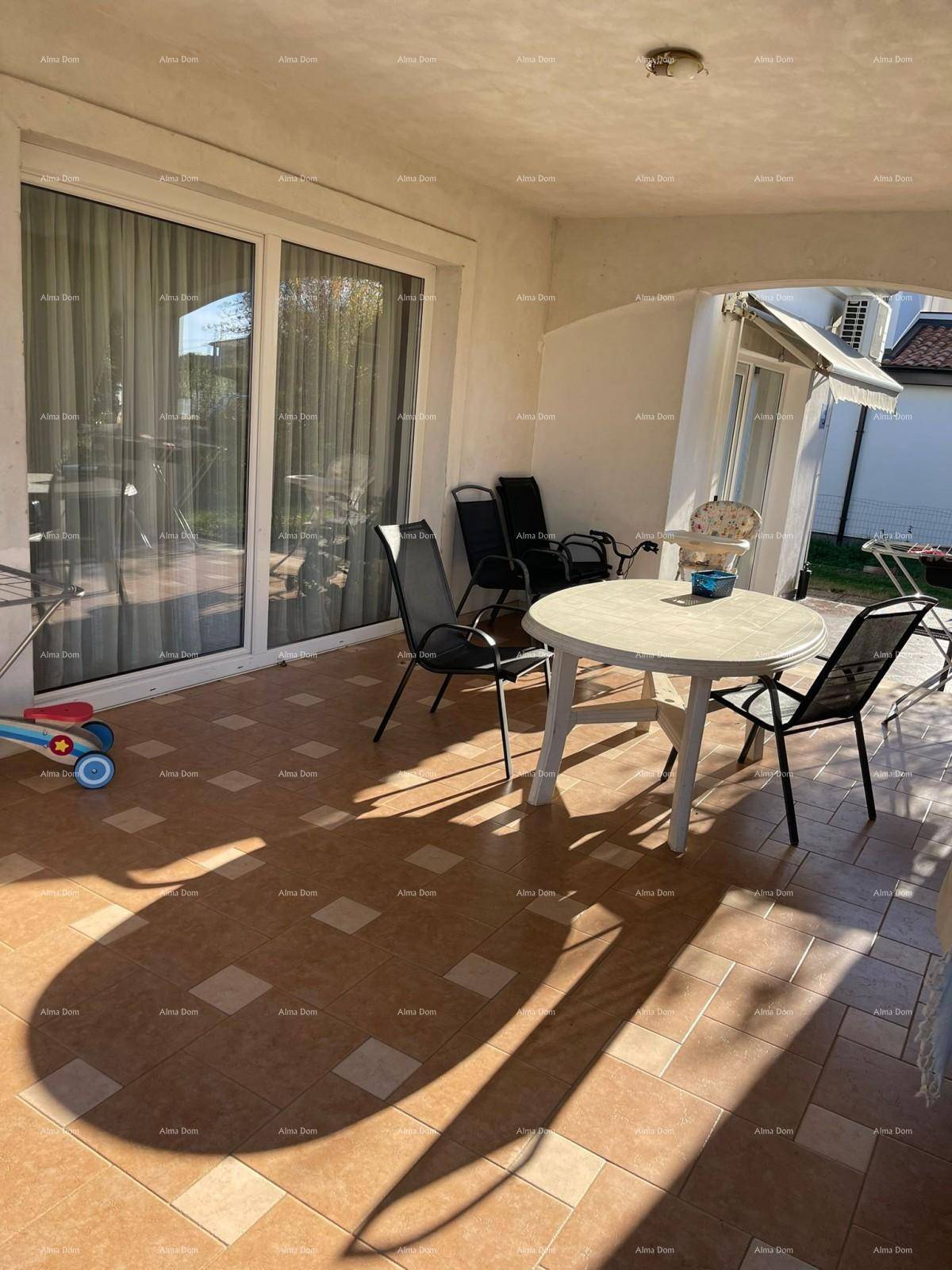 Überdachte Terrasse mit Fliesenboden und Gartenmöbeln, direktem Zugang zum Innenbereich durch Glasschiebetüren.