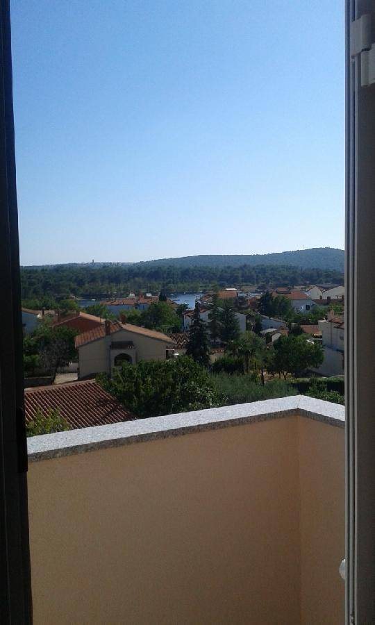 Weitblick vom Balkon über eine Stadt mit roten Dächern und einem See oder Meer in der Ferne. 
