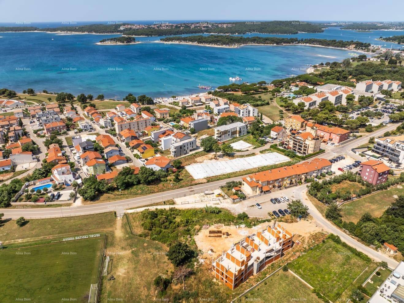 Luftaufnahme einer Küstenstadt mit Wohngebäuden, Straßen und einem im Bau befindlichen Objekt nahe dem Meer.