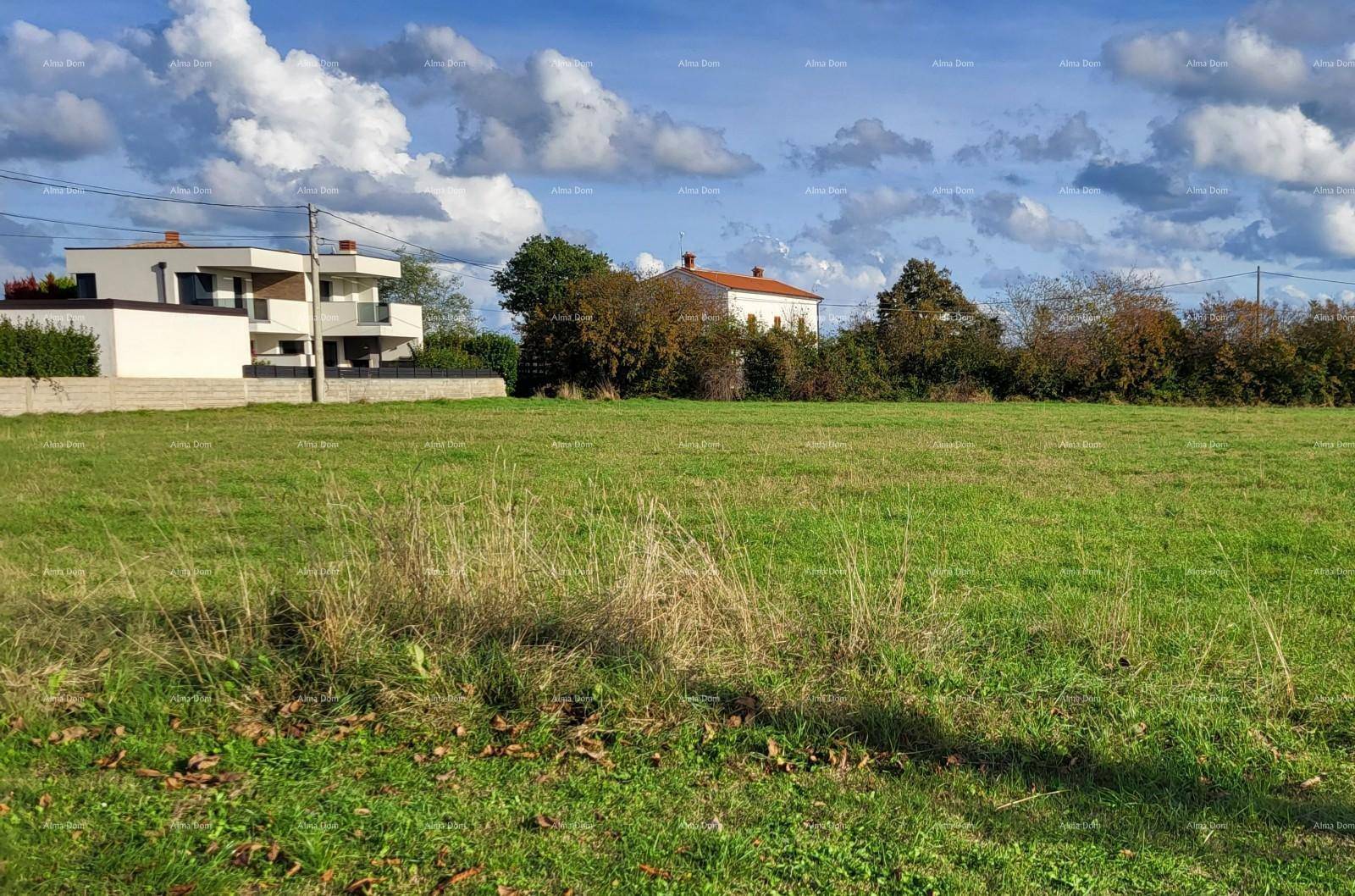 Weitläufiges grünes Grundstück mit Grasfläche und einigen Häusern im Hintergrund unter bewölktem Himmel.