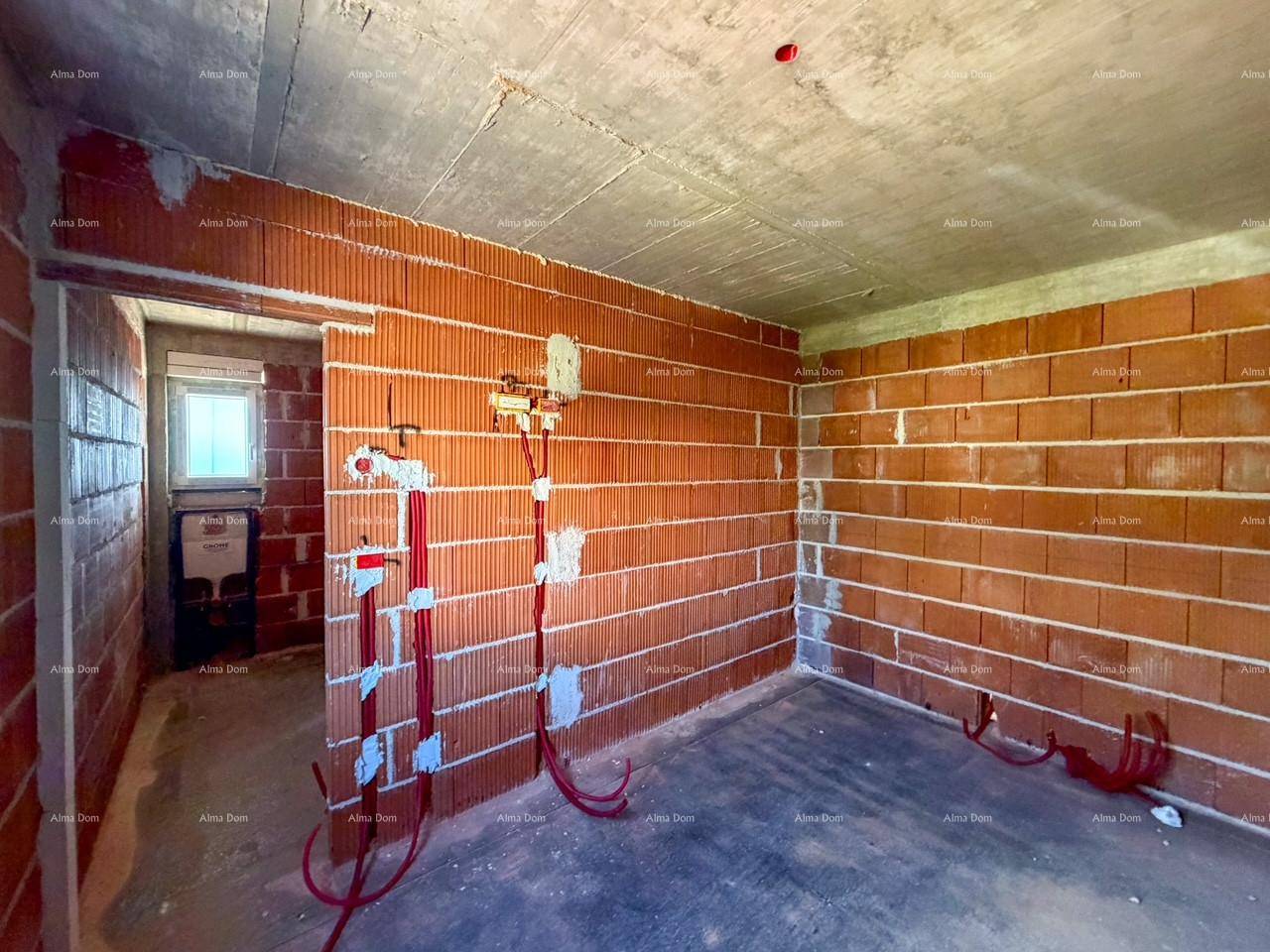 Raum im Rohbau mit Ziegelwänden und vorbereiteten Elektroinstallationen, angrenzend an ein Bad.