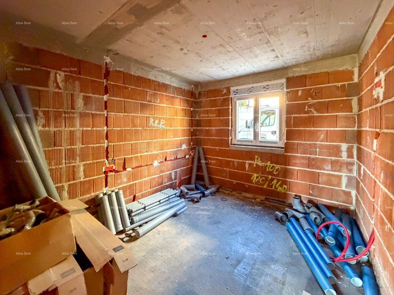 Raum im Rohbau mit Ziegelwänden, einem Fenster und Installationsrohren auf dem Boden.