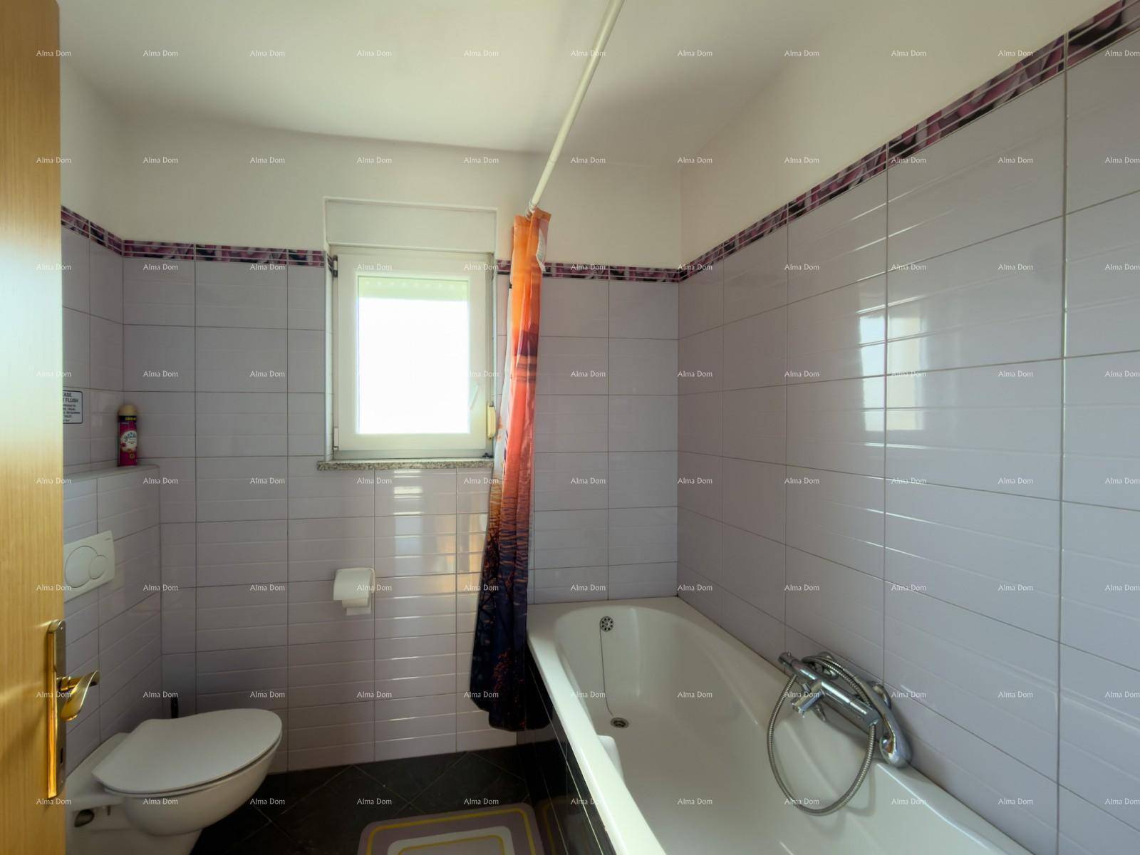 Badezimmer mit Badewanne, WC und Fenster, gefliest in hellen Farbtönen.