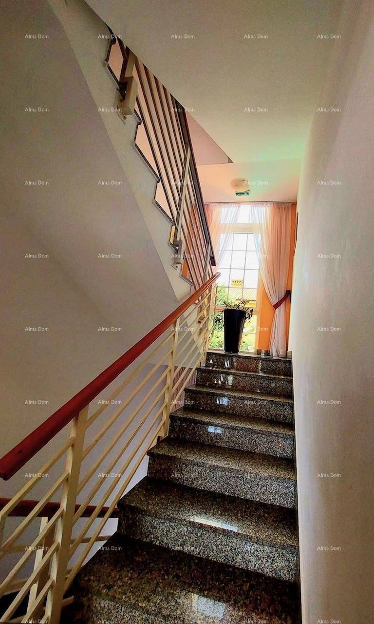 Treppenhaus mit Granitstufen, einem Metallgeländer und einem großen Fenster, das viel Tageslicht hereinlässt.