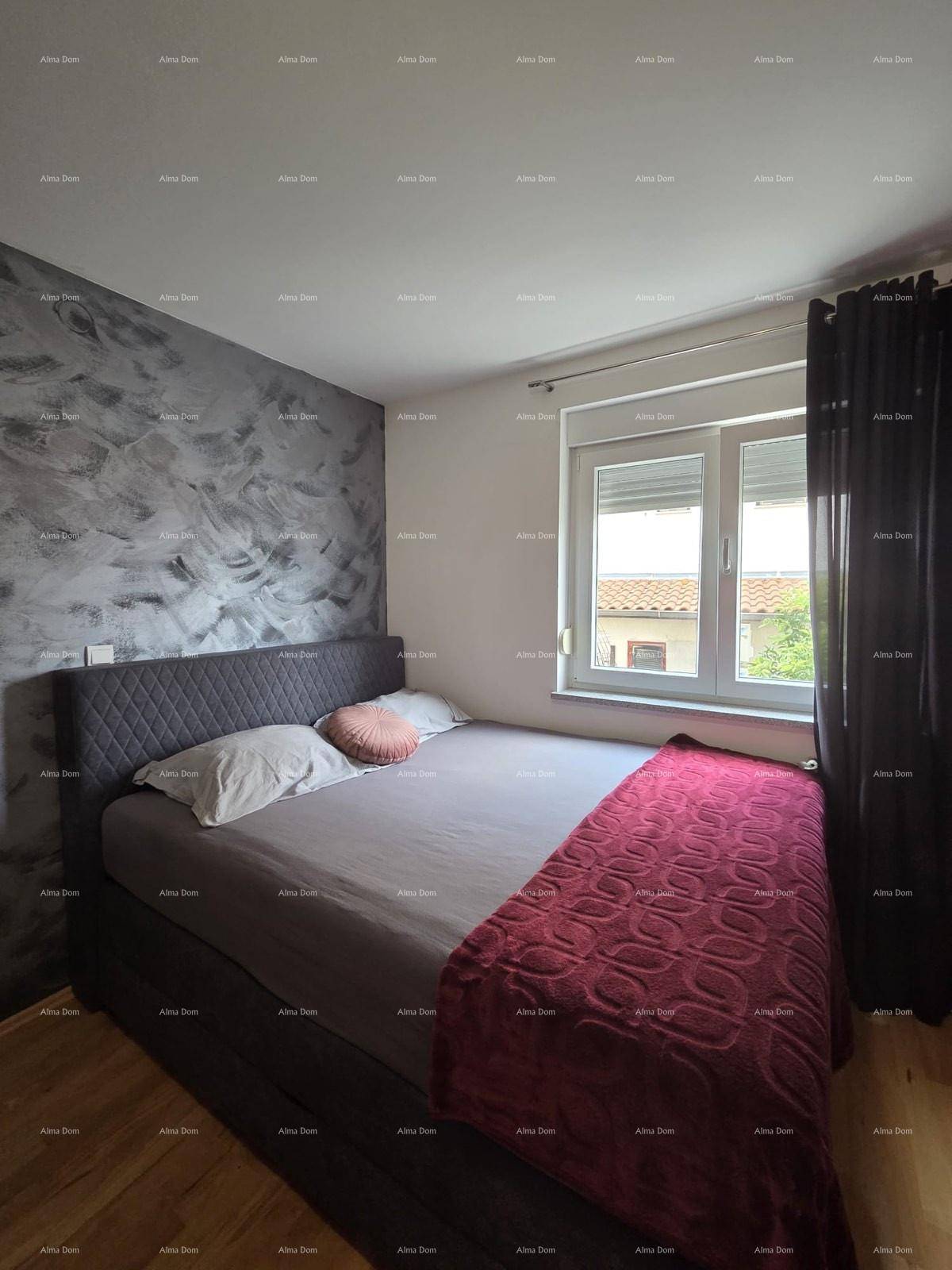 Schlafzimmer mit Doppelbett, dunkler Akzentwand und Holzboden, gut beleuchtet durch ein Fenster.