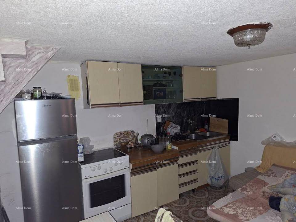 Kleine Küche mit älteren Einbauschränken, Kühlschrank und Herd, integriert in einen Wohnraum.