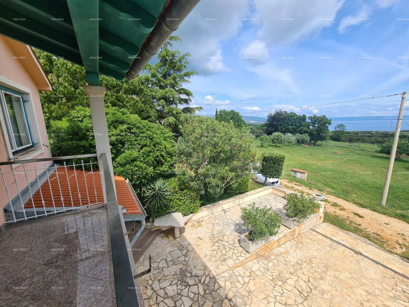 Blick von einem Balkon auf eine Steinterrasse, umgeben von üppigem Grün und dem fernen Meer.