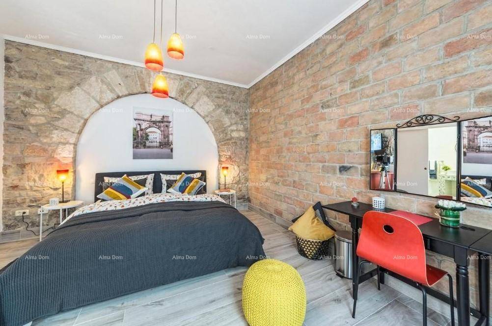 Schlafzimmer mit freigelegter Ziegelwand, Holzboden und einem Schreibtischbereich mit bunter Dekoration.