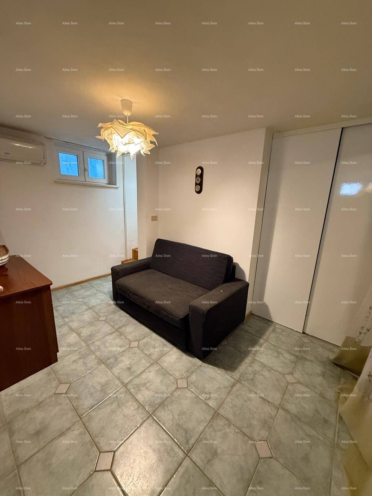 Gemütlicher Wohnbereich mit dunklem Sofa, Fliesenboden und Klimaanlage an der Wand.