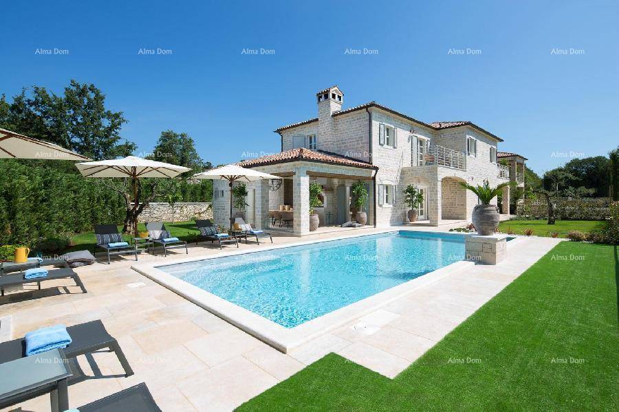 Weitläufiger Poolbereich mit Liegestühlen und der eleganten Steinvilla unter blauem Himmel.