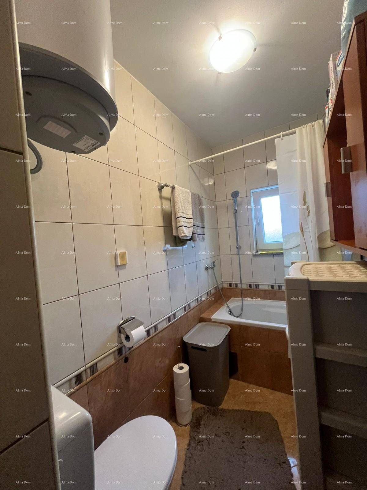 Badezimmer mit Toilette, Badewanne und einem Warmwasserboiler an der Decke.