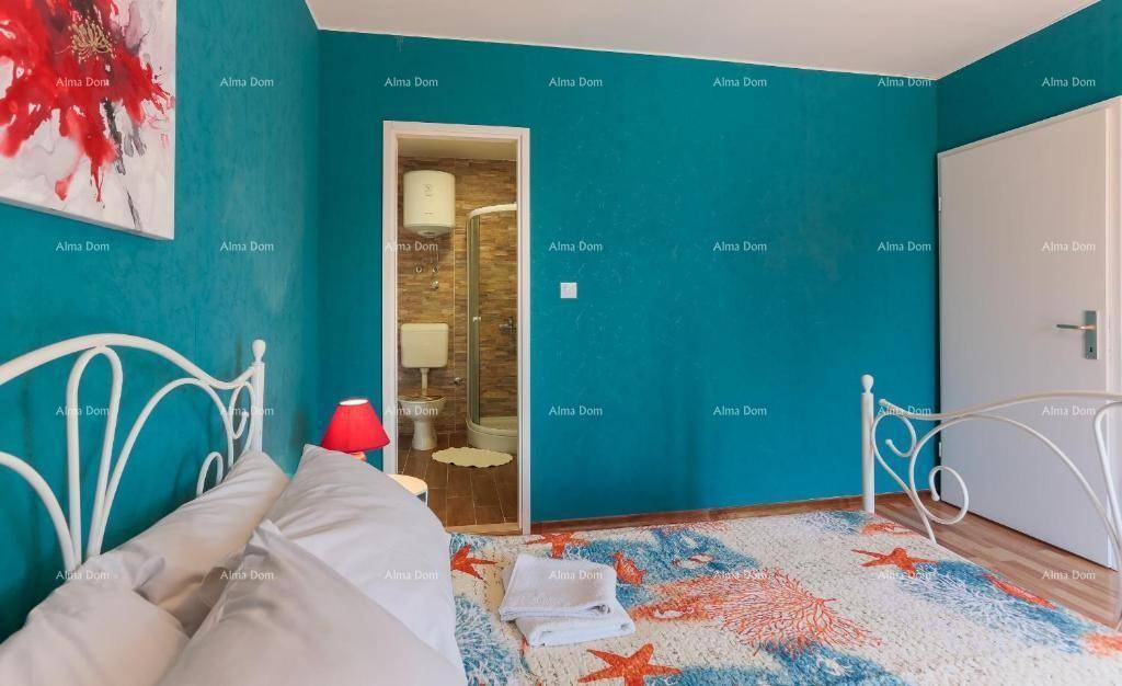 Schlafzimmer mit Doppelbett, blauer Akzentwand und angrenzendem Badezimmer mit Dusche.
