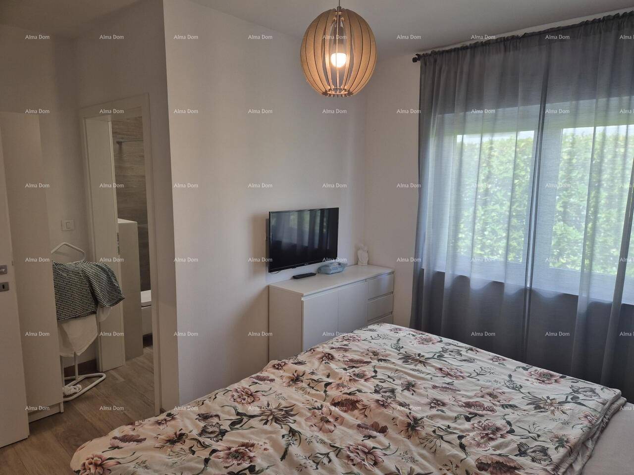 Helles Schlafzimmer mit großem Fenster, Doppelbett und Zugang zu einem angrenzenden Bad.