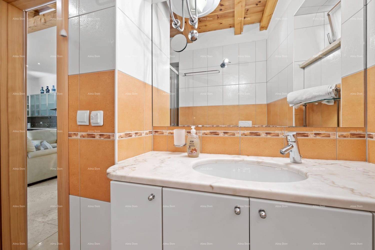 Badezimmer mit Waschtisch, großem Spiegel und orange-weißen Fliesen an den Wänden.