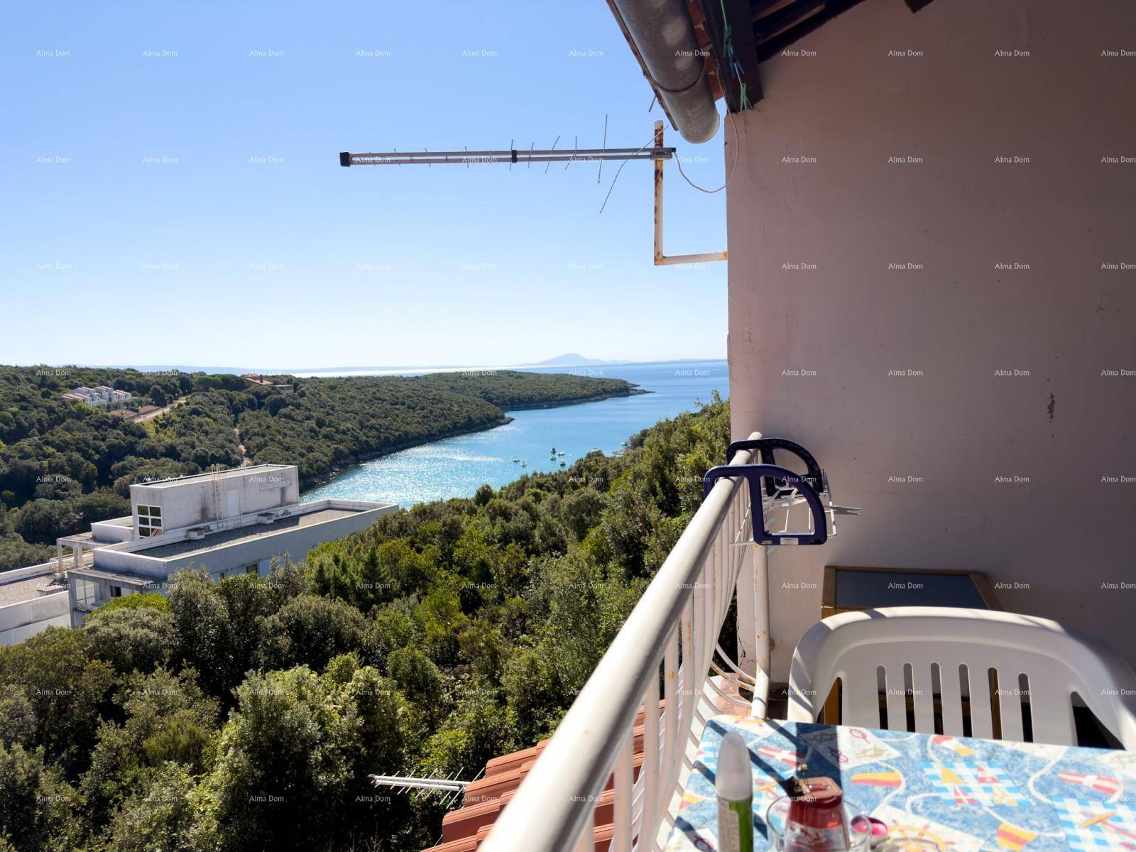 Gemütlicher Balkon mit Tisch und Stühlen, bietet einen weiten Blick über die bewaldete Küste und das Meer.